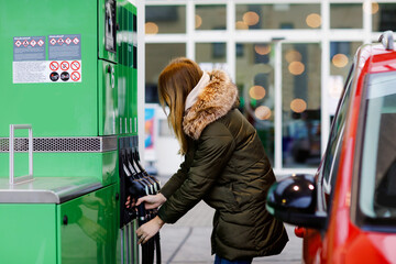 Woman wear medical mask at self-service gas station, hold fuel nozzle, refuel the car with petrol...