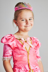 Little girl enjoying her role of princess. Adorable cute 5-6 years old girl wearing pink princess dress and tiara standing on plain background