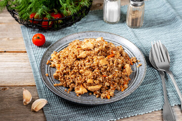 Buckwheat porridge with meat and vegetables in a ceramic plate on a gray wooden table. Buckwheat for a healthy diet