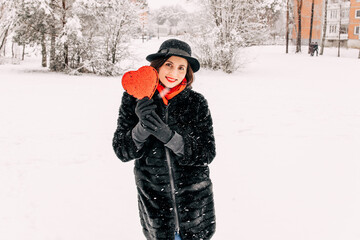 Young woman in winter clothes is having fun outdoors in winter. Snow. Love and leisure concept. Heart with sequins. Saint Valentine's 