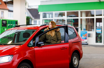 Young attractive woman gets out of her car by gas station to refill car with petrol or gas. People refuel gasoline, driving, transport concept. Self service gas pump