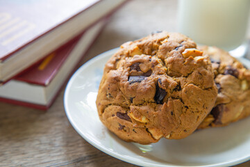 Close up high angle view chocolate chip cookies on a wooden table with a cup of milk next to a books background