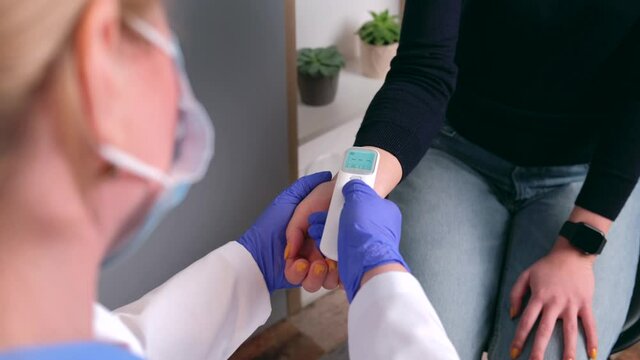 Blonde caucasian doctor wearing a mask is measuring the body temperature of the patient using an electronic thermometer