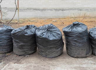Row of black plastic dirty garbage bags near wall
