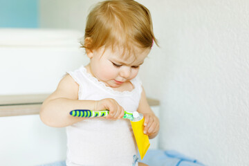 Little baby girl holding toothbrush and brushing first teeth. Toddler learning to clean milk tooth. Prevention, hygiene and healthcare concept. Happy child in bathroom