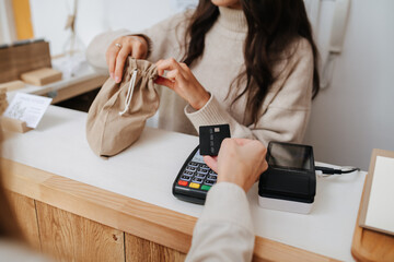 Shopkeeper behind stand with cash register, putting goods in a fabric bag. Female customer making a...