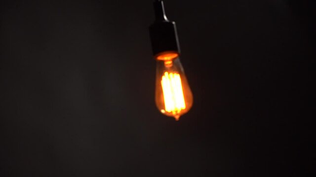 Bulb moves on a wire. Lamp swinging on a black background. Slow motion. Loop 
