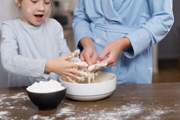 happy mom and cute adorable baby girl cook cookies or pie together, standing at the table in the kitchen. Hands and dough