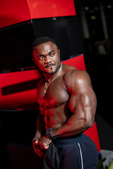 Fototapeta na wymiar Muscular man african bodybuilder. Man posing on a dark gym background. Handsome man shows health and perfect shape.