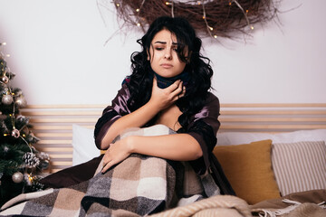 Dark curly hair upset woman lying in bed with scarf sore throat at home. Pretty lady got sick ill...