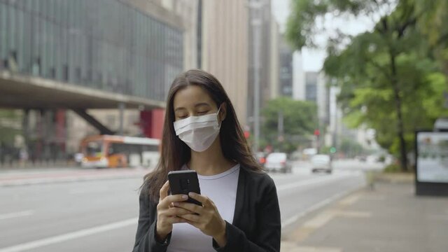  woman walking around paulista avenue wearing face mask using smartphone. Communication, social networks, online shopping concept.
