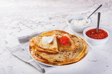 Traditional Russian Crepes Blini stacked in a plate with red caviar, fresh sour cream on light background. Maslenitsa traditional Russian festival meal. Russian food, russian kitchen. Close up.