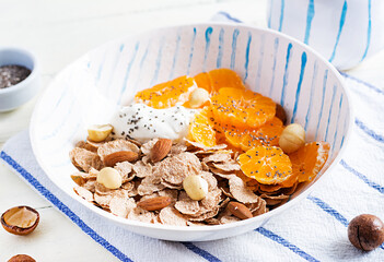 Bowl of flakes with yogurt and tangerine on white wooden table. Fitness food.
