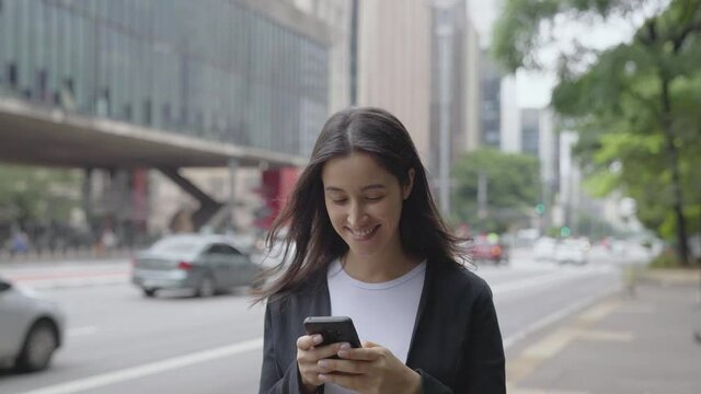 Smiling young woman walking around paulista avenue using smartphone. Communication, social networks, online shopping concept.
