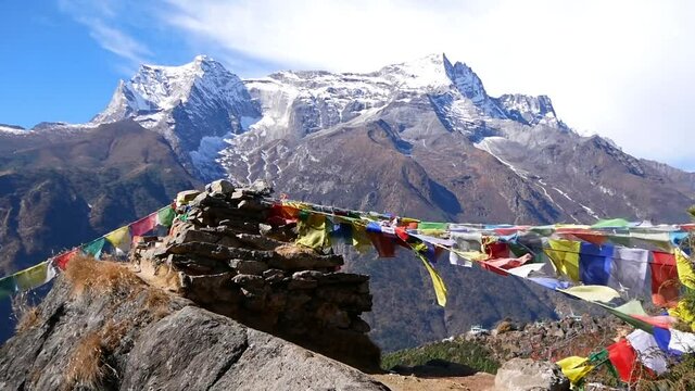Multi-colored Buddhist prayer flags attached to a pile of stones flying in the wind above village Namche Bazar, Khumbu, Himalayas, Nepal with majestic peak of Kongde Ri (6,187 m) in background.