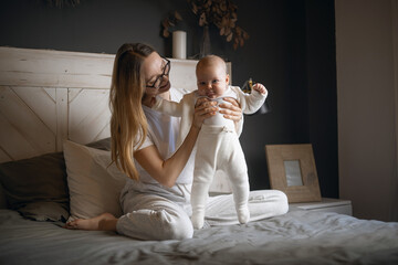 Beautiful mother with her baby. Young beautiful woman looks at her little daughter. Baby girl laughing in her mother's arms.