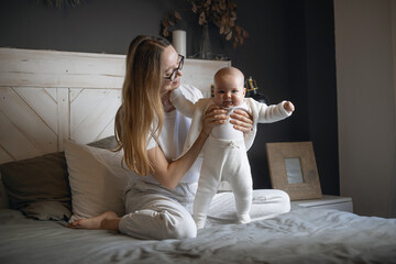 Beautiful mother with her baby. Young beautiful woman looks at her little daughter. Baby girl laughing in her mother's arms.