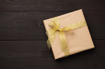 box wrapped in brown paper and tied with a golden ribbon with a bow, gift on a wooden background