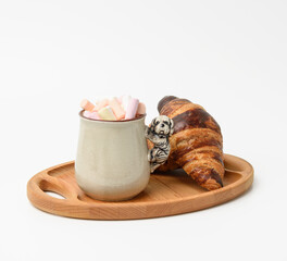 ceramic mug with cocoa and marshmallows, baked croissant on a wooden serving plate