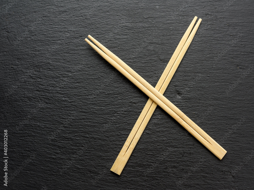 Wall mural two wooden sticks for sushi on a black background