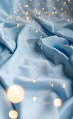 Background of garlands with bokeh lights on the folds of fabric in blue color. Copy space. Romantic aesthetic Valentines day concept background