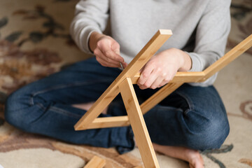 Teen boy assembles furniture according to the instructions - a wooden chair. Housework and order in it. Lesson for a teenage boy on vacation. Assistant.