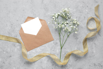 Blank card mockup in a envelope, gypsophila flowers and a gold ribbon. Gray concrete grunge...