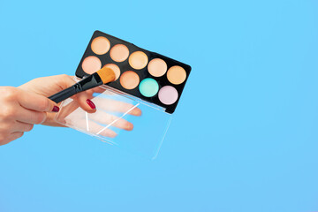 Female hand holding cosmetic palette against blue background