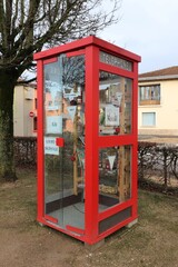 Fototapeta na wymiar Ancienne cabine téléphonique rouge transformée en point d'échange de livres, ville de Polliat, département de l'Ain, France