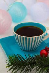 Black coffee in a blue with a christmas tree branch cup around garland of balloons