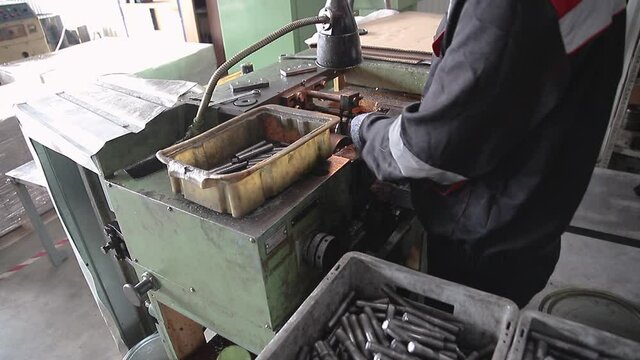 worker makes metal stud with thread on thread rolling machine, the production process of the part on the machine