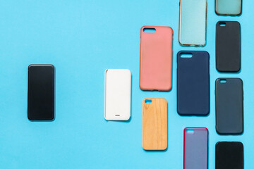 Pile of multicolored plastic back covers for mobile phones on blue background with a phone on the side