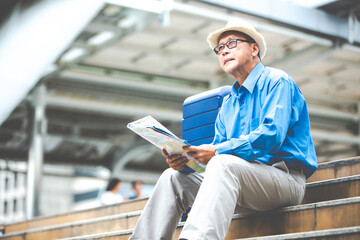 Senior man traveling with luggage sitting on staircase checking city map and sightseeing Travel and tourism concept.Elderly Travel and tourism concept.