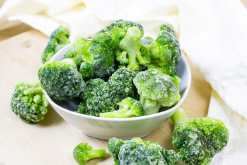 Fresh green frozen broccoli in small white bowl on light background.