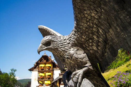 Imposing metal eagle statue under a clear blue sky. A German Black Forest house is in the background.