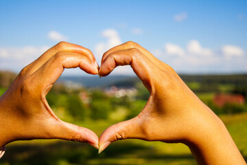 Close-up of woman's hands forming a heart in the golden evening sun. If you look through you can...