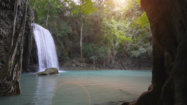 waterfall clear emerald water or blue pool with spa fish on summer with rock and tree for relax travel in green jungle or forest at erawan waterfall floor 3 for nature landscape on sunlight flare slow