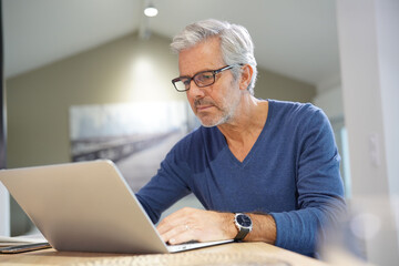 Senior man with eyeglasses connected with laptop at home
