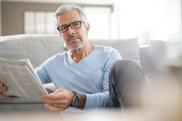 Attractive senior man with eyeglasses relaxing at home reading newspaper