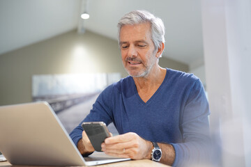 Portrait of senior man with blue shirt using smartphone and laptop