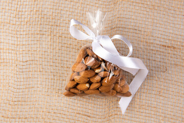 almonds in a gift transparent package tied with a white ribbon on a burlap on a white background