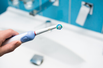 Electric oscillating toothbrush in woman hand in bathroom at home