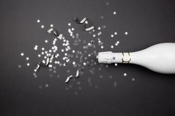 Champagne bottle and confetti on dark background. Flat lay of celebration composition. Top view. Copy space.