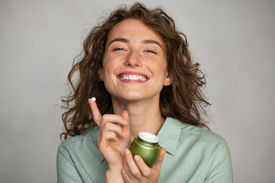 Beautiful smiling woman applying facial cream from green jar