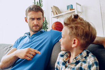 Father is having a talk with his little son while sitting on couch at home