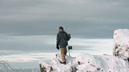 Snowboarder reaches at the peak of the snowed in mountain and looks into the valley 