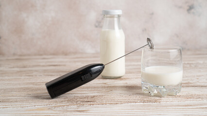 Frother and milk on light wooden table. Milk in bottle. Milk handheld mixer