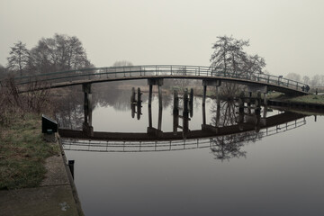 Beautiful curved bridge on a windless winter day, with a beautiful reflection of the bridge in the water, photo taken at the nature reserve 