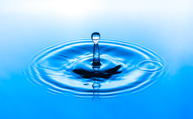 Water drop splashing into blue water surface. Health and purity concept