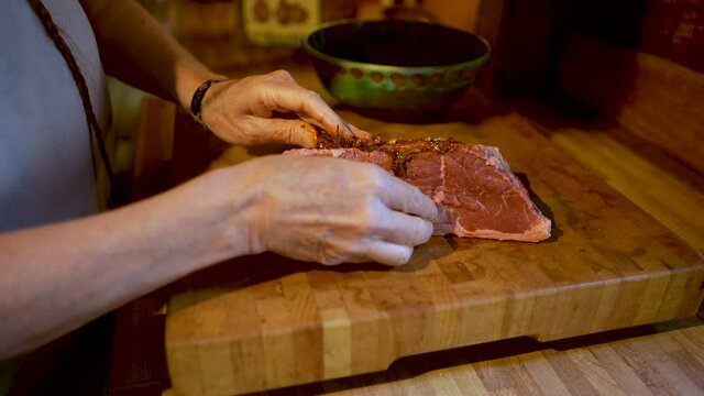Woman putting marinade on a cut of steak on a wooden cutting board
